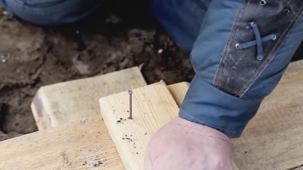 Человек вбивает гвоздь в деревянные доски, крупным планом, на открытом воздухе — стоковое видео