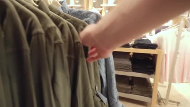 Escolhendo roupas da moda na loja, verificando a qualidade do material. Conceito de compras para camisas e camisetas, jaquetas, fundo — Vídeo de Stock