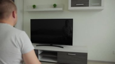 Adam salonda oturup LCD TV 'de film izliyor. Haberler, spor programı, film. Uzaktan kumanda elinde. Evdeki kanepede ev eğlencesi. Canlı yayın. Modern iç daire. Rahatla.