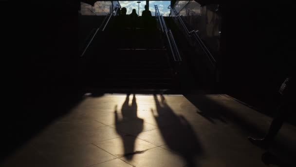 人々は地下鉄、地下鉄の地下通路、日没の階段の近くの暗い地下道を歩く。シルエット。地下鉄への回廊。旅行や都市生活の概念、抽象 — ストック動画