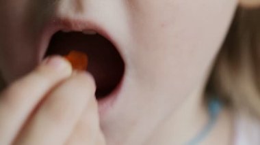Küçük bir kız, ayı şeklinde vitamin yiyor. Çocuk sağlığını multivitamin kompleksleriyle güçlendirme kavramı. Yakın plan.