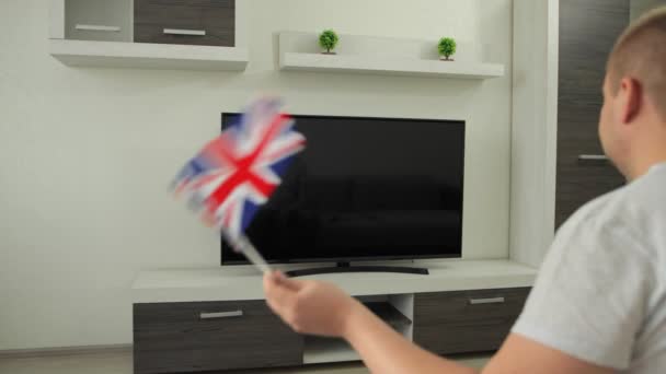 Sportovní fanoušek sedí doma před televizí, mává vlajkou Velké Británie a oslavuje vítězství týmu v soutěži v letních zimních hrách. Muž se dívá na vysílání mistrovství světa. Win UK — Stock video