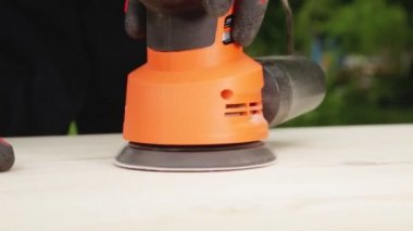 Bir adam ahşabı elektrikli bir aletle cilalıyor, yakın plan. El yapımı ahşap, zımpara kağıdıyla ahşap temizleme.