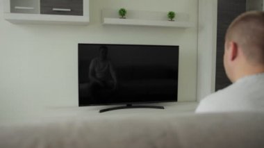 Adam salonda oturuyor ve LCD TV 'de haberleri izliyor. Spor müsabakası, film. Hayranım. Canlı yayın. Uzaktan kumanda elinde. Evdeki kanepede ev eğlencesi. Modern iç daire. Bahis