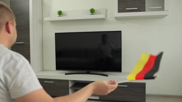 O torcedor de esporte senta-se em casa em frente à TV, acena a bandeira da Alemanha e celebra a vitória da equipe nacional na competição de eventos de Jogos de Inverno de Verão. Homem assiste transmissão de Copa do Mundo. Ganhar — Vídeo de Stock