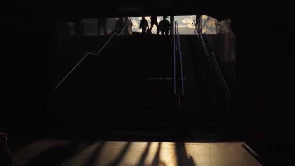 Les gens marchent à travers le passage souterrain sombre près des escaliers au susnet, passage souterrain, métro. Silhouette. Couloir vers le métro. Concept de voyage et de vie urbaine, abstrait — Video