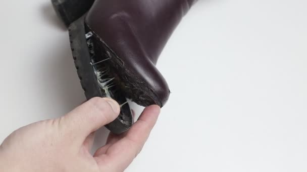 Ένας τεχνίτης παπουτσιών κολλά το πέλμα μιας γυναικείας χειμερινής μπότας. Χαμηλής ποιότητας παπούτσια έννοια, μπότες επισκευής, close-up — Αρχείο Βίντεο