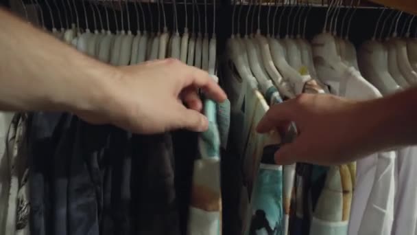 Het kiezen van modieuze kleding in de winkel, het controleren van de kwaliteit van het materiaal. Winkelconcept voor shirts en T-shirts, jassen, achtergrond — Stockvideo
