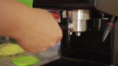 Bir adam kahve makinesinin fişini çekip temizliyor ve yeni bir kahve ekliyor, yakın plan.