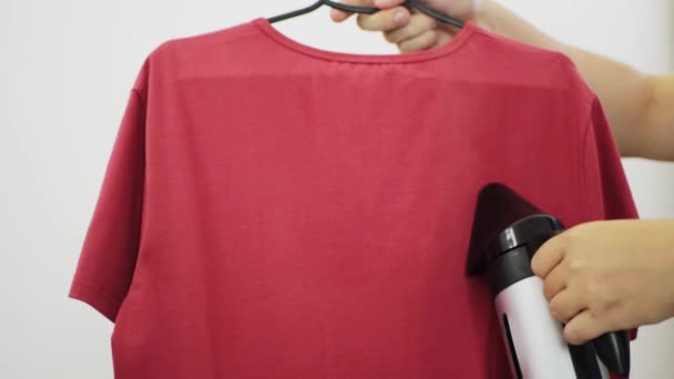 Ånga den röda T-shirten på en rynkhängare. Strykjärn, närbild — Stockvideo