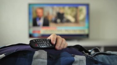 Adam uyuyor, televizyonun uzaktan kumandası karnında yatıyor. Uyu. Haberler, politik kanal. Uyu. Yorgunluk, yorgunluk. Adam evdeki kanepede uzanıyor ve televizyon izlemiyor.