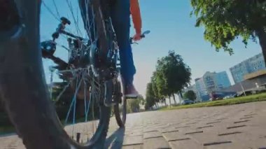 Adam şehirde MTB bisikleti sürüyor. Tekerlek yakın çekim. Zincirleme sürüş, arka raydan çıkarıcı ve kaset. Dağ bisikletinin vitesi. Jokey tekerlekleri, aylak aylak aşağı ve yukarı makaralı. Cogset dişlileri. Vites değiştir.