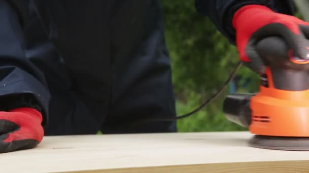 Un homme polit le bois avec un outil électrique, un gros plan. Bois fait à la main, nettoyage du bois avec du papier de verre — Video