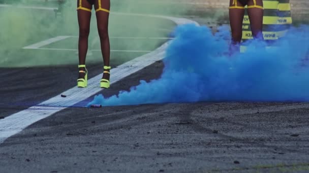 En färgad blå rökbomb ligger på asfalten och röker under bilens drift racing tävlingar. Ben av animatörflickor. Motorsport mästerskapet. Närbild. Professionell extrem drift — Stockvideo
