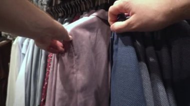Bir erkek mağazada şık kıyafetler, ceketler, gömlekler ve tişörtler seçer. Arkaplan, yakın plan, alımlar
