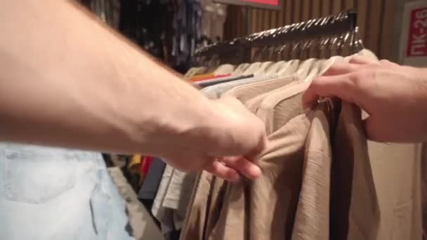 Мужчина выбирает модную одежду, куртки, рубашки и футболки в магазине. Предпосылки, крупный план, покупки — стоковое видео