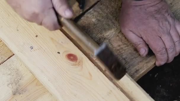 Workman σφυρηλατεί ένα καρφί σε ξύλινες σανίδες, κοντινό πλάνο, σε εξωτερικούς χώρους — Αρχείο Βίντεο