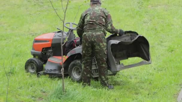 Un uomo ripara un trattore per tagliare l'erba. Campo verde con erba fresca estiva, primo piano — Video Stock