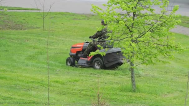 Ouvrier embauché tondre l'herbe au printemps dans le jardin sur une tondeuse à essence automotrice, tracteur pour tondre l'herbe, fond. Industrie — Video