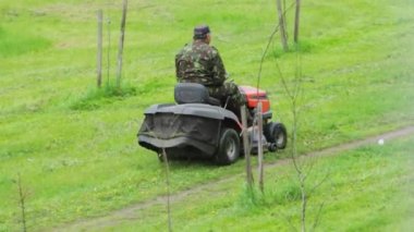 Bir erkek işçi yazın çimleri kendi kendini iten bir çim biçme makinesiyle biçiyor. Yeşil çimen tarlası, açık hava