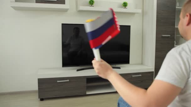 Sport fan sits at home in front of TV. Russia vs USA. Rooter waves national flags and watches broadcast of Summer Winter games event competition, world championship cup — Stockvideo