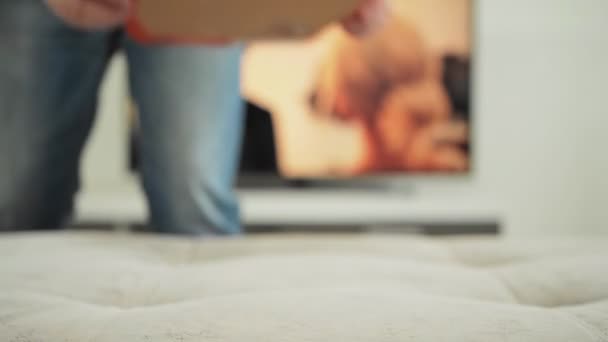 L'uomo mette una pizza sul divano davanti alla TV. Mangia e guarda un film a casa. Nutrizione nociva e stile di vita. Fine settimana, ferie, fine settimana lavorativa. — Video Stock