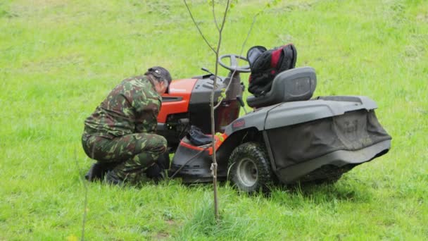 Un uomo ripara un trattore per tagliare l'erba. Campo verde con erba fresca estiva, primo piano — Video Stock