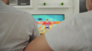 İki erkek taraftar evdeki kanepede oturur ve televizyonda spor müsabakaları izlerler. Yaz oyunu yarışması. Ağırlık 2021. Rooters meraklıları modern iç mekanlarda plazma yayını izliyorlar. Akıyor. Varım. Tokyo