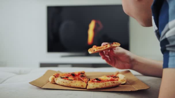 Chubby leży na kanapie, ogląda film w telewizji i je pizzę. Szkodliwy styl życia i odżywiania. Koncepcja depresji i samotności. Weekend, wakacje, koniec tygodnia pracy. — Wideo stockowe