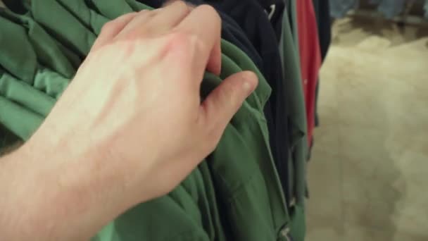 Een man kiest modieuze kleding, jassen, shirts en T-shirts in de winkel. Achtergrond, close-up, aankopen — Stockvideo