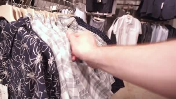 在商店里挑选时髦的衣服，检查材料的质量。衬衫、 T恤衫、夹克、背景的购物概念 — 图库视频影像