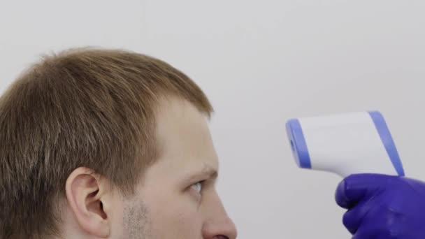 Het meten van de lichaamstemperatuur met een elektronische thermometer bij een blanke man op een witte achtergrond. Concept van preventie van virale ziekten, close-up — Stockvideo