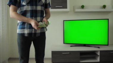 Man counts euro money in his hands at home. Focus on TV. Green screen chromakey. Betting concept, bet. Financial and investment success in crypto coin currency market. Modern interior apartment room