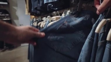 Bir erkek mağazadan kot pantolon seçer. Giysi alışverişi konsepti, yakın çekim, moda.