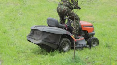 A male worker sits on a tractor and starts mowing grass. Self-propelled petrol lawn mower, close-up