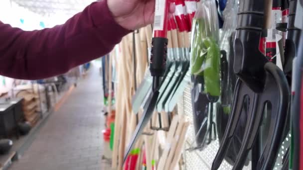 A man chooses garden products in the department of a hypermarket. Garden shovels for planting plants, close-up — Video