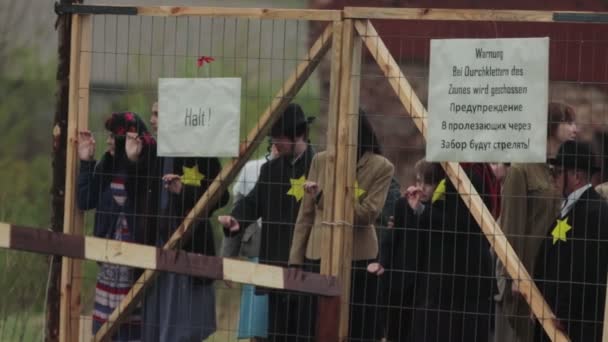 Jewish prisoners stand behind a fence in a concentration camp during reconstruction of events of World War II. Yellow star of David is sewn on clothes. BOBRUISK, BELARUS - MAY 9, 2021 — Vídeo de Stock