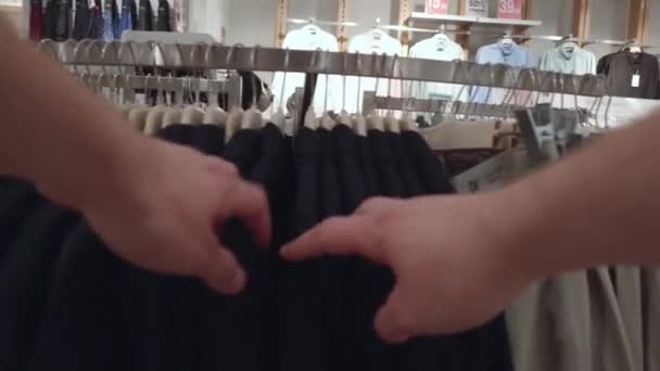 En man väljer kläder i en affär och handlar. Urval av T-shirts och jackor i butiken, bakgrund, närbild — Stockvideo