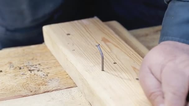 Een man slaat een gebogen spijker in houten planken, close-up. Beroep — Stockvideo