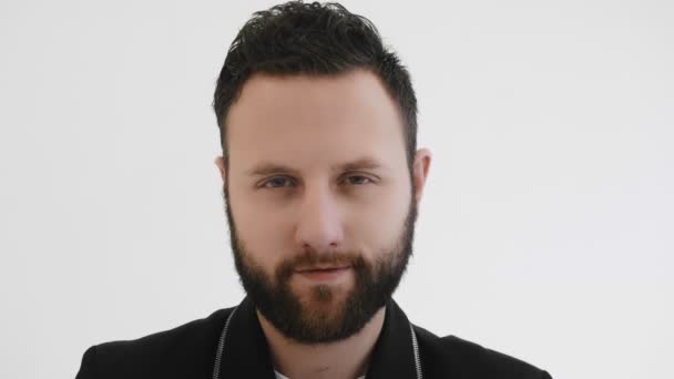 Fashionable stylish man moves his eyes around. Portrait of bearded brutal guy looking to camera. Trendy fancy person narrowed his eyes. Black jacket. Chic, modish. White background in studio. Closeup — Stock Video