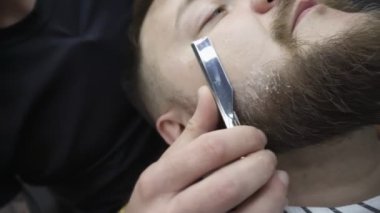 Berber salonu içinde. Paslanmaz çelik kenarlı, tıraş bıçağı kesen berber tombul müşterinin sakalını keser. Tımar, saç kesimi ve tıraş hizmeti. - Yakın çekim. Beyaz adam.