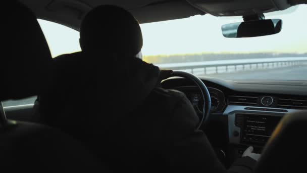 Un autista di sesso maschile in giacca e cappello guida un'auto in inverno in autostrada. Un raggio del sole tramontante splende attraverso la finestra, viaggio. Lento mo — Video Stock