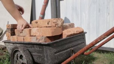Bir erkek işçi taşımacılık için kırmızı bir bina tuğlasını el arabasına monte ediyor. Kırsaldaki DIY İnşaat, arka plan. Yakın plan.
