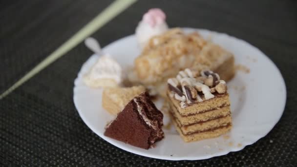 Sütemények és torták maradványai egy tányéron az asztalon. Káros ízletes édes étel. Közelkép — Stock videók