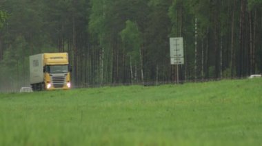 Yarı römorklu sarı bir vagon yağmurlu ve nemli yaz havasında kargo taşır. Yük ve lojistik konsepti