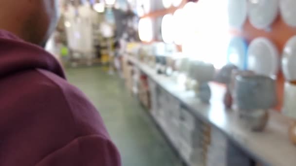 Um homem escolhe uma lâmpada de iluminação no departamento elétrico de uma loja de ferragens, fundo, close-up — Vídeo de Stock