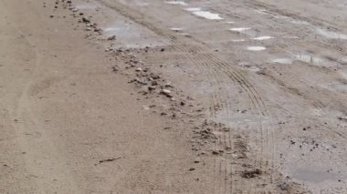 Arka planda çukurlar ve su birikintileri olan kötü çakıl yolu. Sonbaharda kayalar ve toprak kırılan kumlu yol, manzara