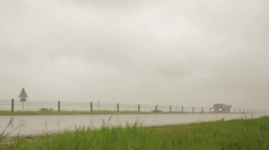 40 tonluk yükü olan turuncu 4 eksenli bir kargo kamyonu yazın arka planda ıslak bir yolda gidiyor. Toplu kargo taşımacılığı, kötü hava