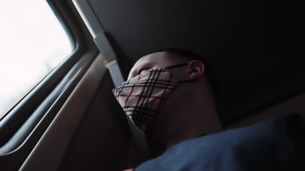 Een man met een medisch beschermend masker reist in een treinwagon en kijkt uit het raam. Corovirus epidemie tijdens een trein om te rusten, close-up — Stockvideo