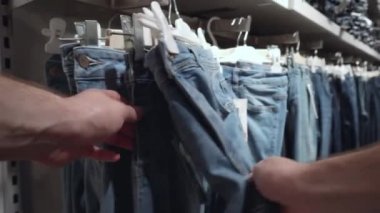 Bir erkek mağazadan kot pantolon seçer. Giysi alışverişi konsepti, yakın çekim, moda.
